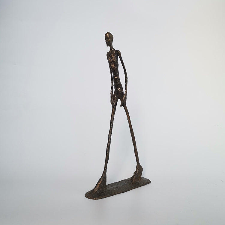 Bronze sculpture of a long-legged figure on a white background