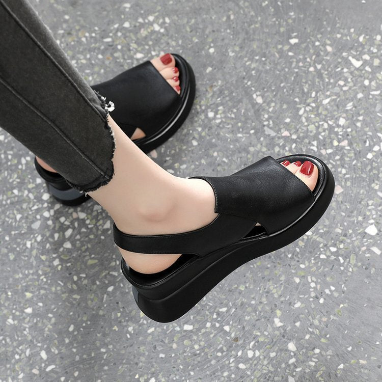 Black platform sandals worn on a gray pavement surface