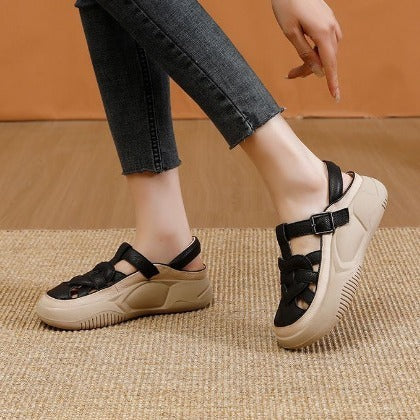 Black and beige sandals worn with black jeans on a textured surface.