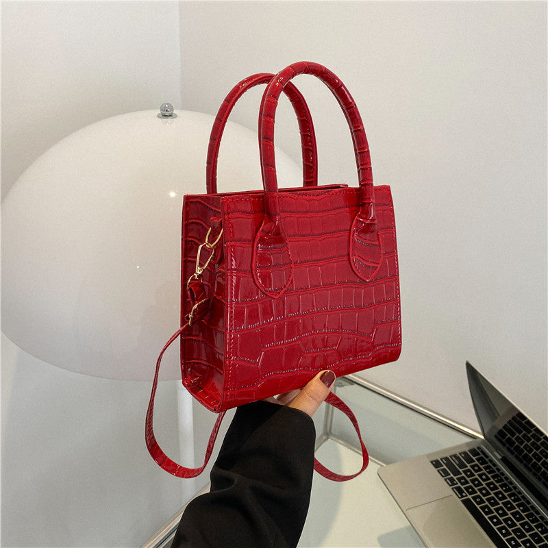 Red crocodile-patterned handbag held by a person with a white background