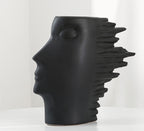 Black vase shaped like a stylized face with spiky hair on a white background