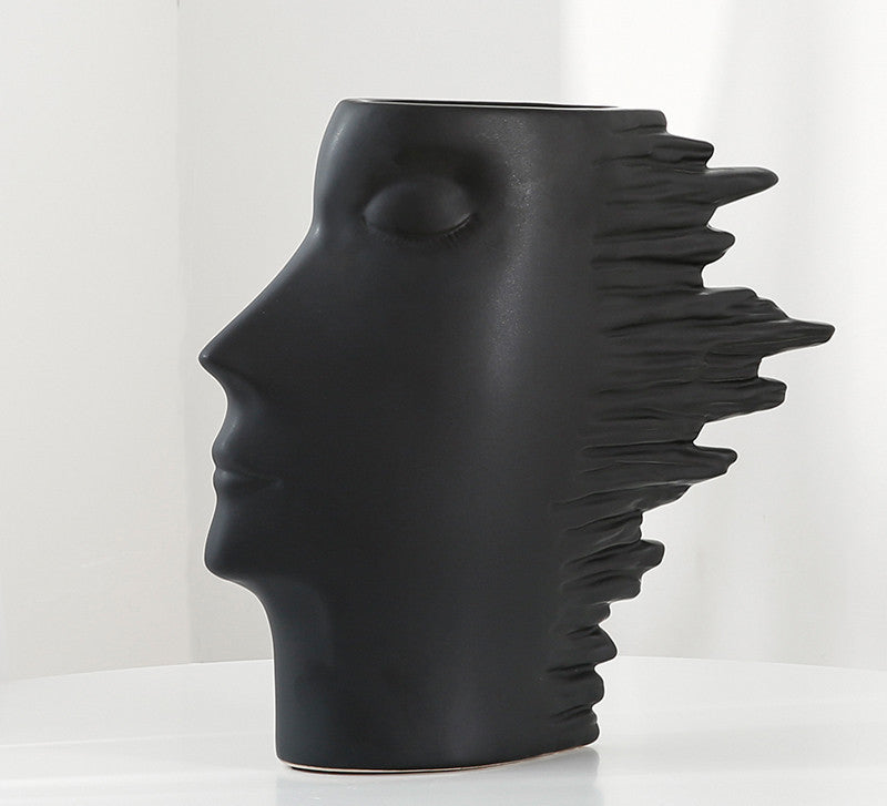 Black vase shaped like a stylized face with spiky hair on a white background