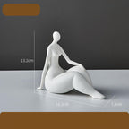White ceramic sculpture of a sitting figure with dimensions on a gray surface.