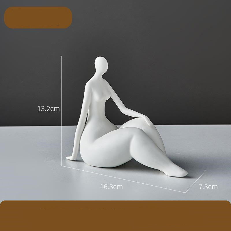 White ceramic sculpture of a sitting figure with dimensions on a gray surface.