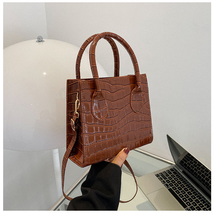 Brown textured handbag held in front of a laptop on a white surface