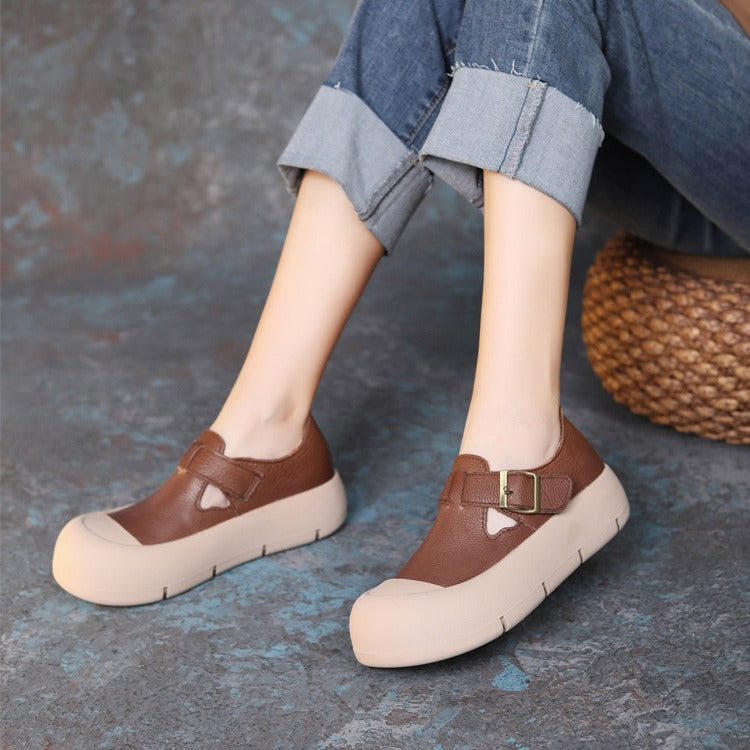 Brown shoes with beige soles worn by a person sitting on a textured surface.