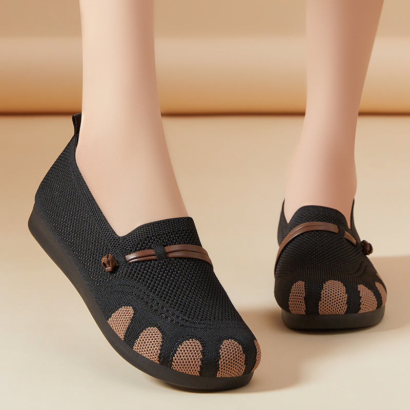 Black open-toe shoes with brown accents worn by a person on a beige background