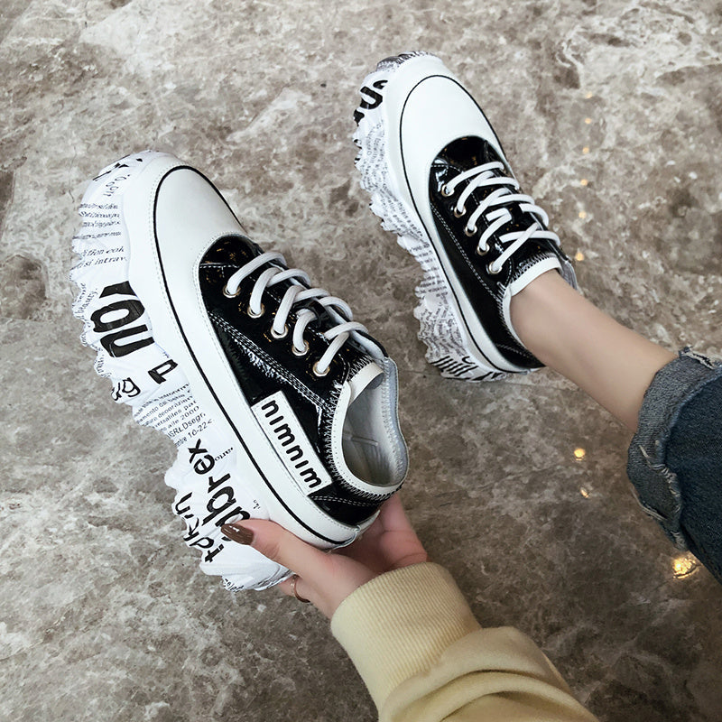 Black and white sneakers with text design held by a person on a textured surface