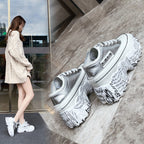 Silver sneakers with text design on a concrete floor, with a person wearing similar shoes in the background.