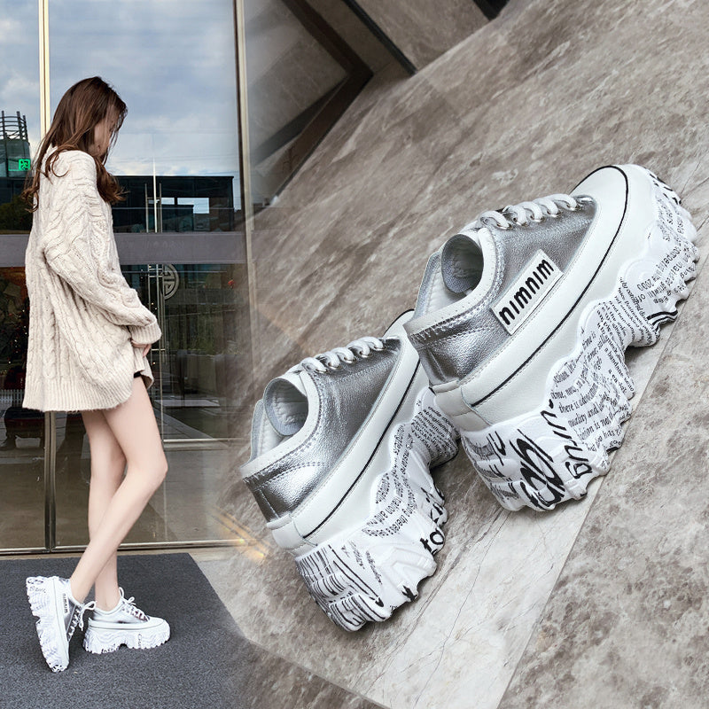 Silver sneakers with text design on a concrete floor, with a person wearing similar shoes in the background.