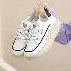 White sneakers with black accents held by a hand against a beige background