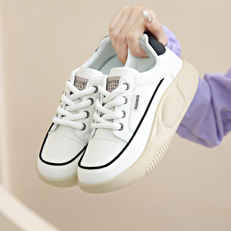 White sneakers with black accents held by a hand against a beige background
