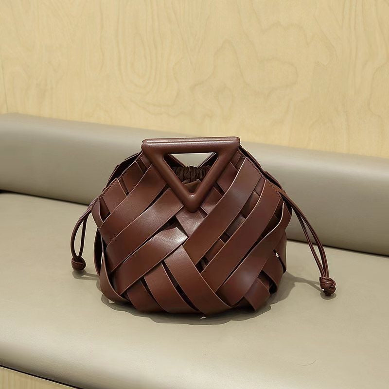 Brown  leather handbag with a triangular handle on a beige surface.