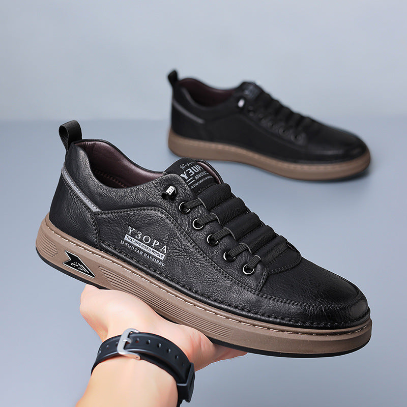 Black leather sneakers with brown soles held by a hand on a gray background