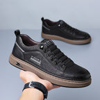 Black leather sneakers with brown soles held by a hand on a gray background