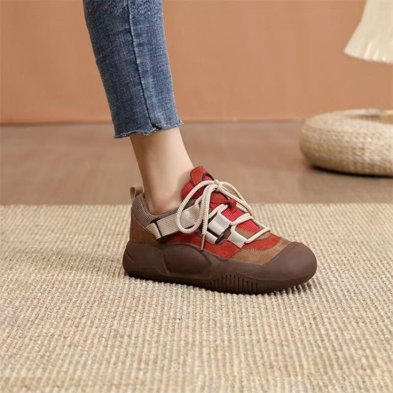 Brown and red sneaker worn indoors on a textured floor.