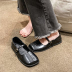 Black shoes with buckles worn by a person on a carpeted floor.