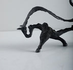 Black metal sculpture of a creature with outstretched wings on a white background