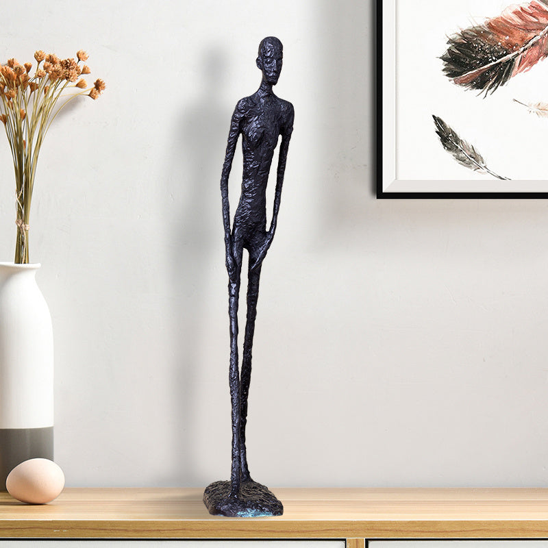 Decorative black sculpture on a wooden surface with a vase and artwork in the background.