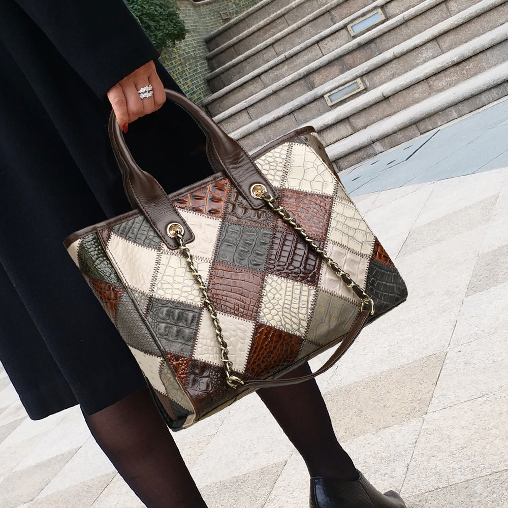 Patchwork handbag with a chain detail held by a person on a tiled pavement.