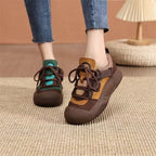 Brown and orange sneakers worn with blue jeans on a textured floor.