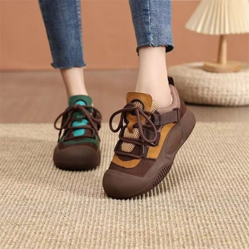 Brown and orange sneakers worn with blue jeans on a textured floor.