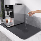 Coffee machine with a black mat on a white countertop, showing water spillage.