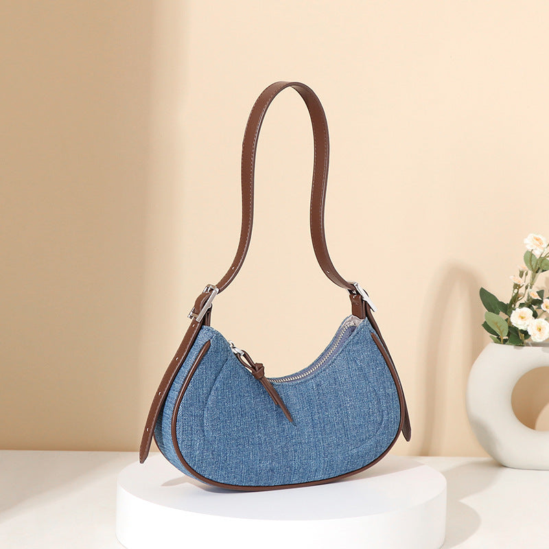 Blue denim handbag with brown leather strap on a beige background