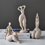 Three ceramic sculptures of people in various poses on a surface with books in the background.