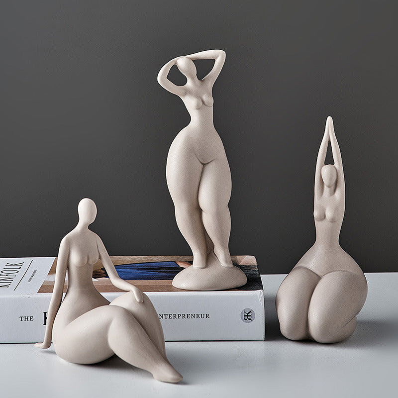 Three ceramic sculptures of people in various poses on a surface with books in the background.