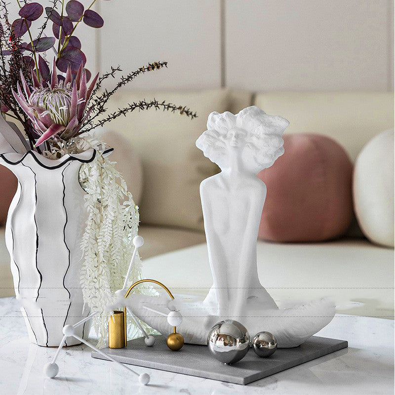Decorative statue on a table with a vase and plants in the background