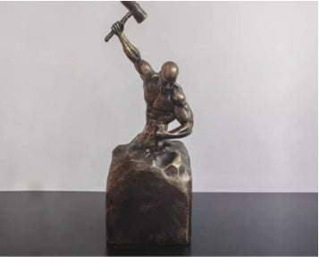 Bronze sculpture of a figure holding a hammer on a gray background