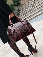 Brown embossed handbag held by a person on a city street.