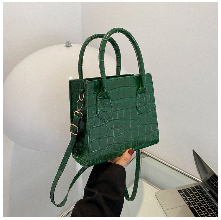 Green crocodile-patterned handbag held by a person with a laptop in the background.