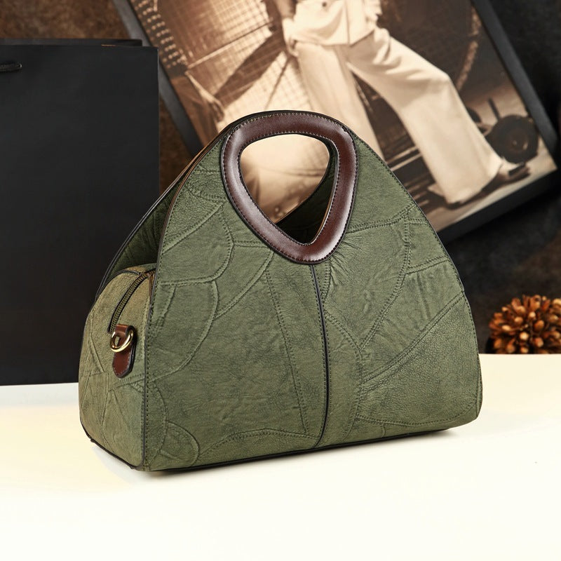 Green handbag with brown handle on a white surface, blurred background