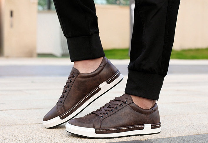 Brown sneakers with white soles worn by a person on a blurred outdoor background