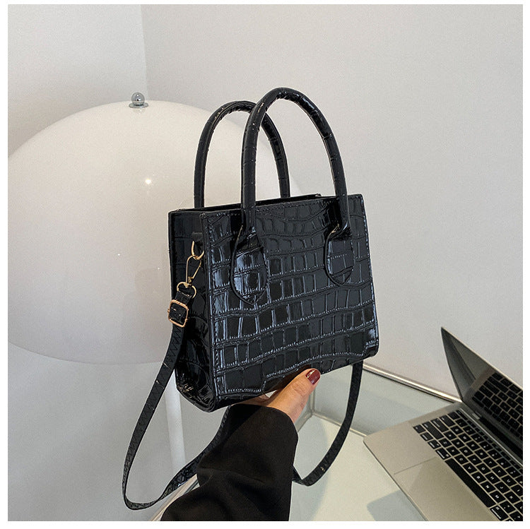 Black crocodile-patterned handbag held by a hand with a white background