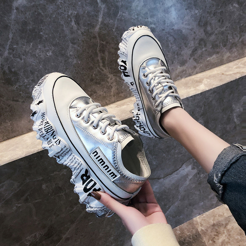 White sneakers with ruffled details held by a person on a stone floor.
