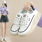 White sneakers with black accents held by a person against a neutral background