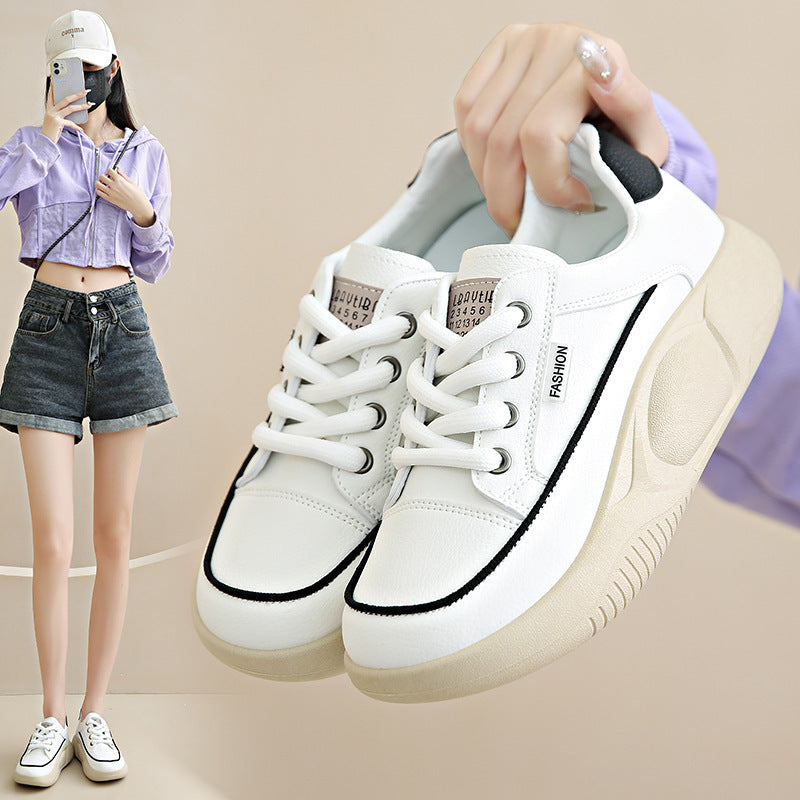White sneakers with black accents held by a person against a neutral background