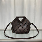 Brown woven handbag on a reflective surface with a light gray curtain background