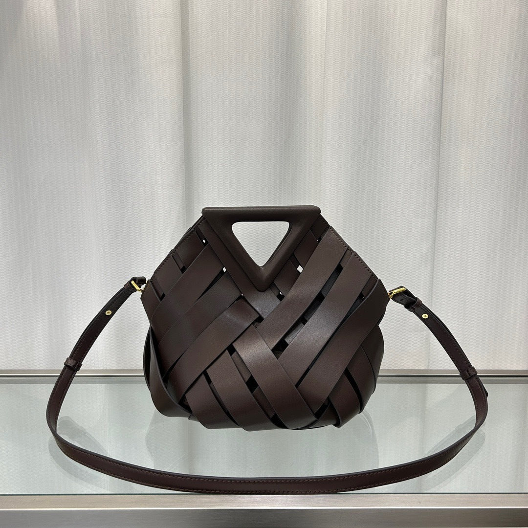 Brown woven handbag on a reflective surface with a light gray curtain background