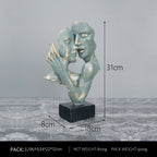 Abstract sculpture of two faces on a gray surface with measurements indicated.