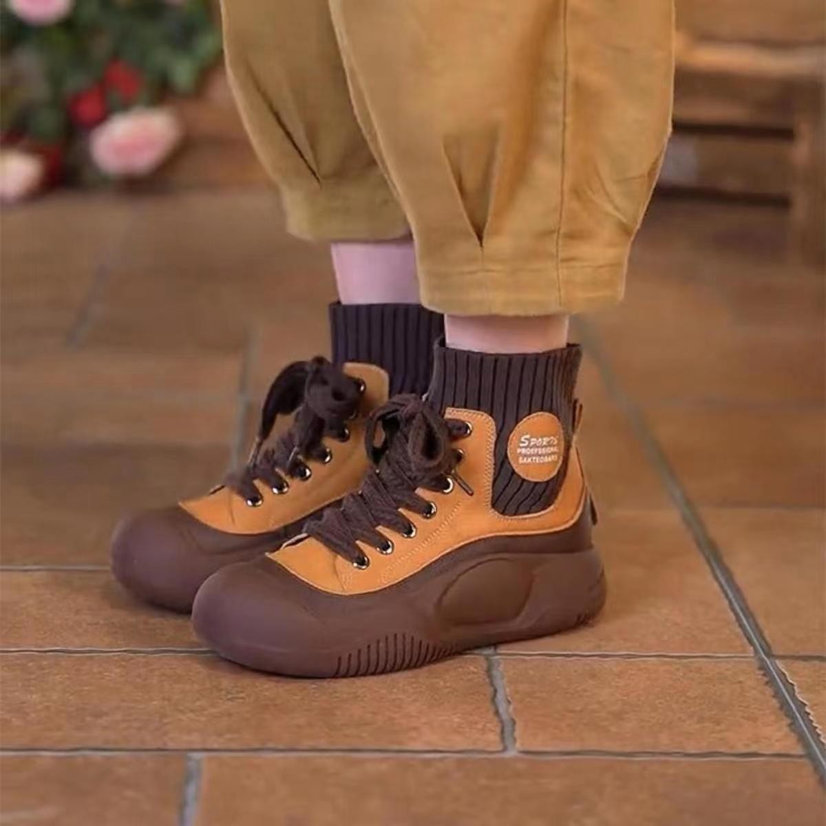 Brown and orange boots worn with yellow pants on a tiled floor.
