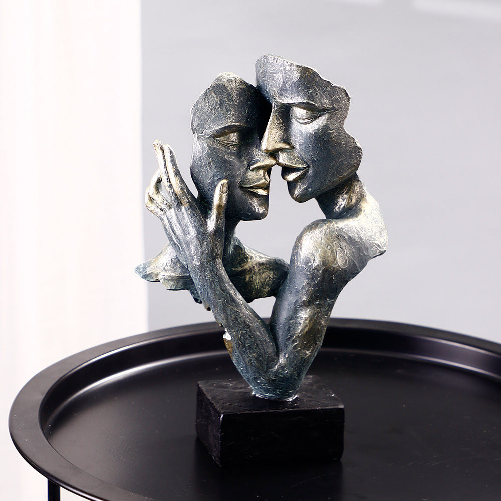 Bronze sculpture of two faces embracing on a black base against a gray background