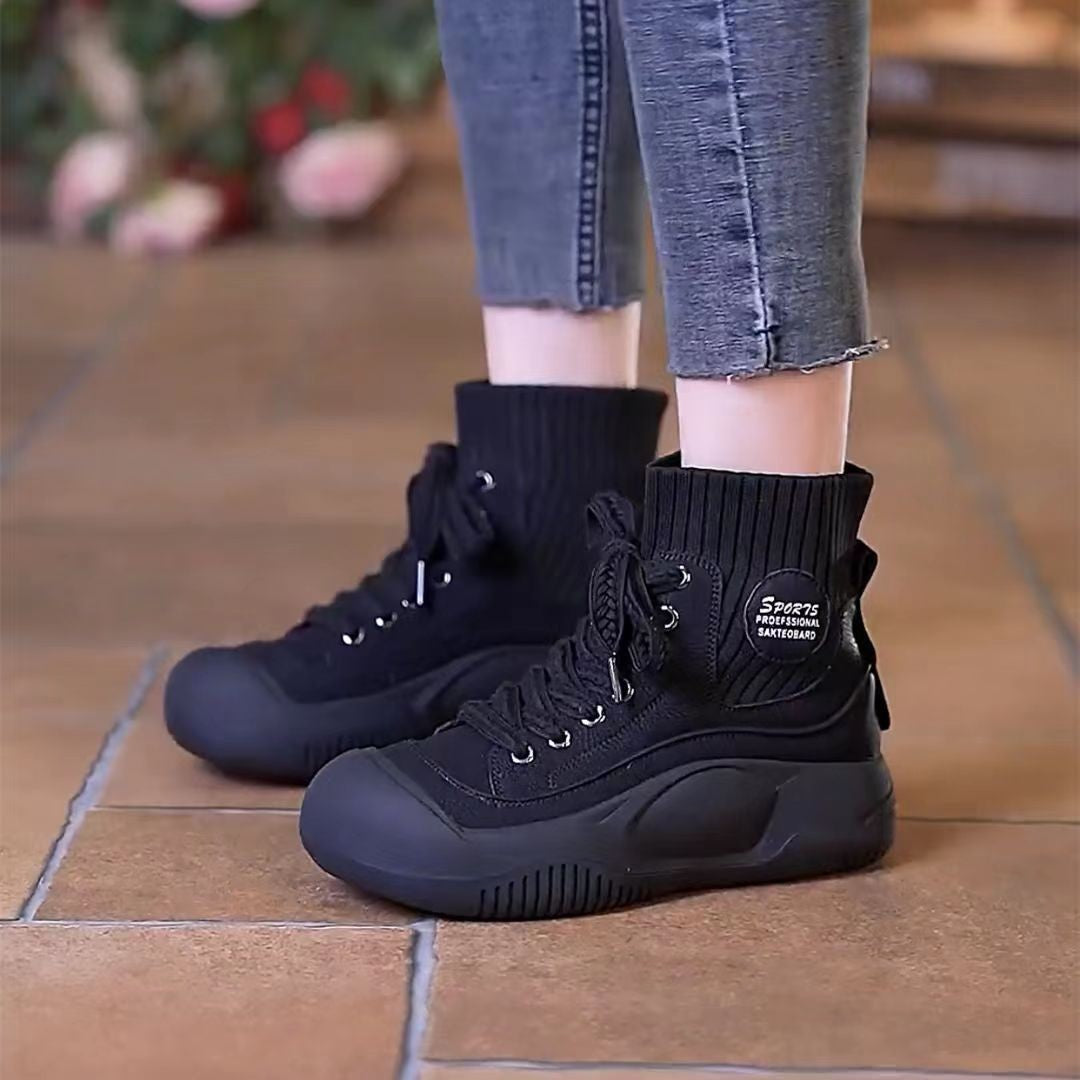 Black high-top sneakers worn with rolled-up jeans on a tiled floor.