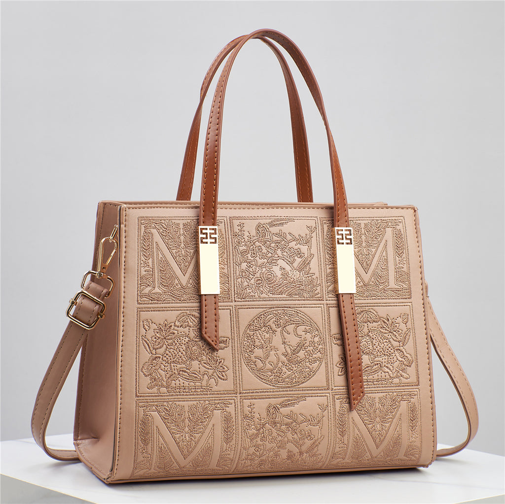 Brown leather handbag with embossed patterns and gold accents on a light gray background