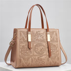 Brown leather handbag with embossed patterns and gold accents on a light gray background