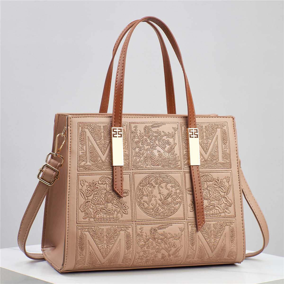Brown leather handbag with embossed patterns and gold accents on a light gray background