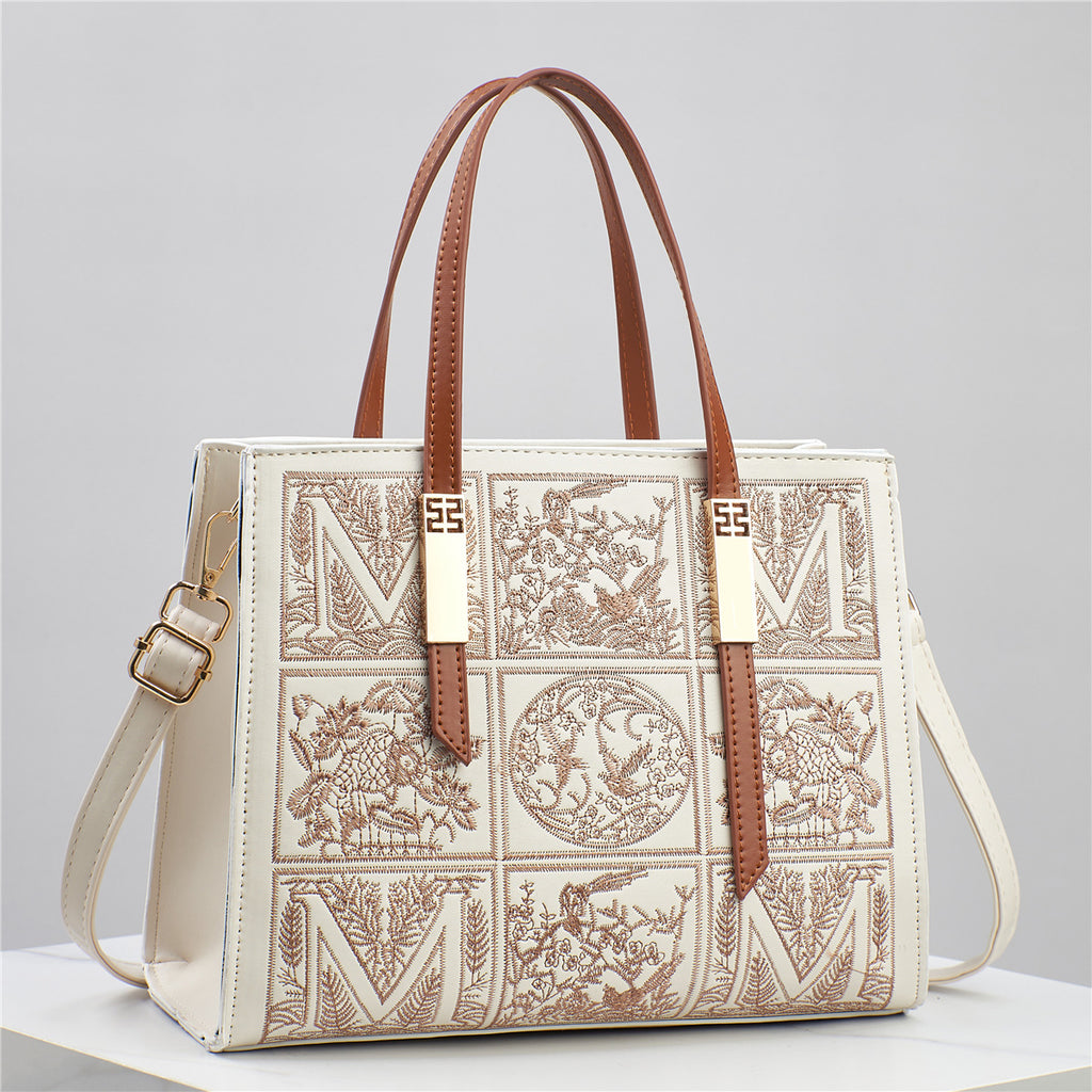Designer handbag with intricate patterns and brown straps on a light gray background